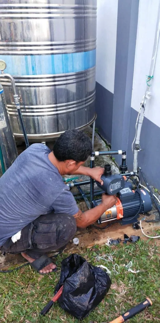 Technician repairing a water pump beside a rooftop storage tank